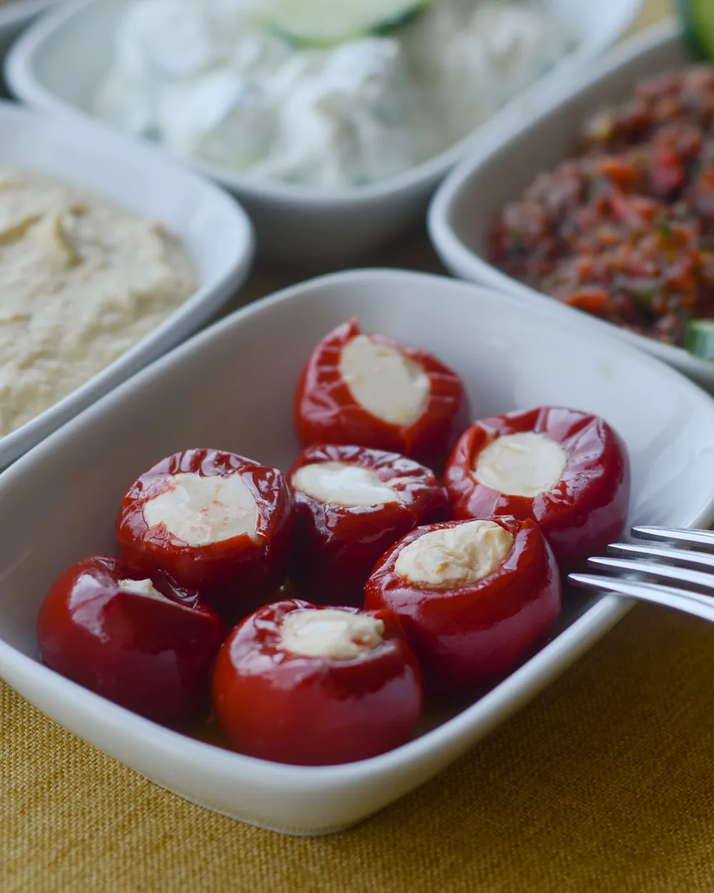 Gefüllte rote Paprika, Hummus und andere kleine Gerichte in weißen Schalen auf einem Tisch – eine Meze-Platte